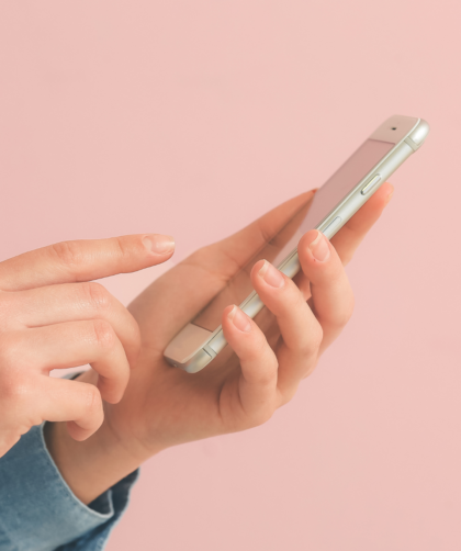 Dłonie w dżinsowej koszuli trzymające smartfon na różowym tle – zdjęcie ilustrujące scrollowanie social mediów i proces rezygnacji z Facebooka oraz Instagrama.