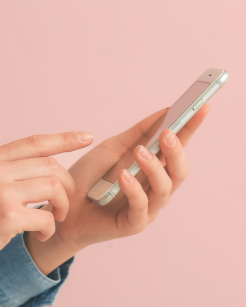 Dłonie w dżinsowej koszuli trzymające smartfon na różowym tle – zdjęcie ilustrujące scrollowanie social mediów i proces rezygnacji z Facebooka oraz Instagrama.