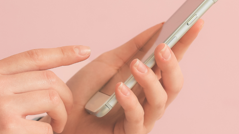 Dłonie w dżinsowej koszuli trzymające smartfon na różowym tle – zdjęcie ilustrujące scrollowanie social mediów i proces rezygnacji z Facebooka oraz Instagrama.