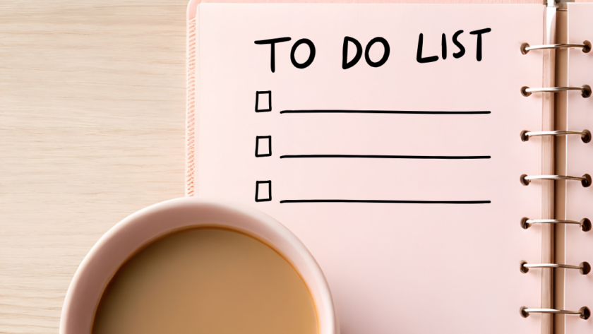 Różowy notatnik z napisem TO DO LIST i puste linie do wypełnienia leżące obok filiżanki herbaty z mlekiem na jasnym drewnianym stole.